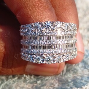 May include: A wide silver band ring with multiple rows of sparkling diamonds. The ring features a combination of round and baguette-shaped diamonds.