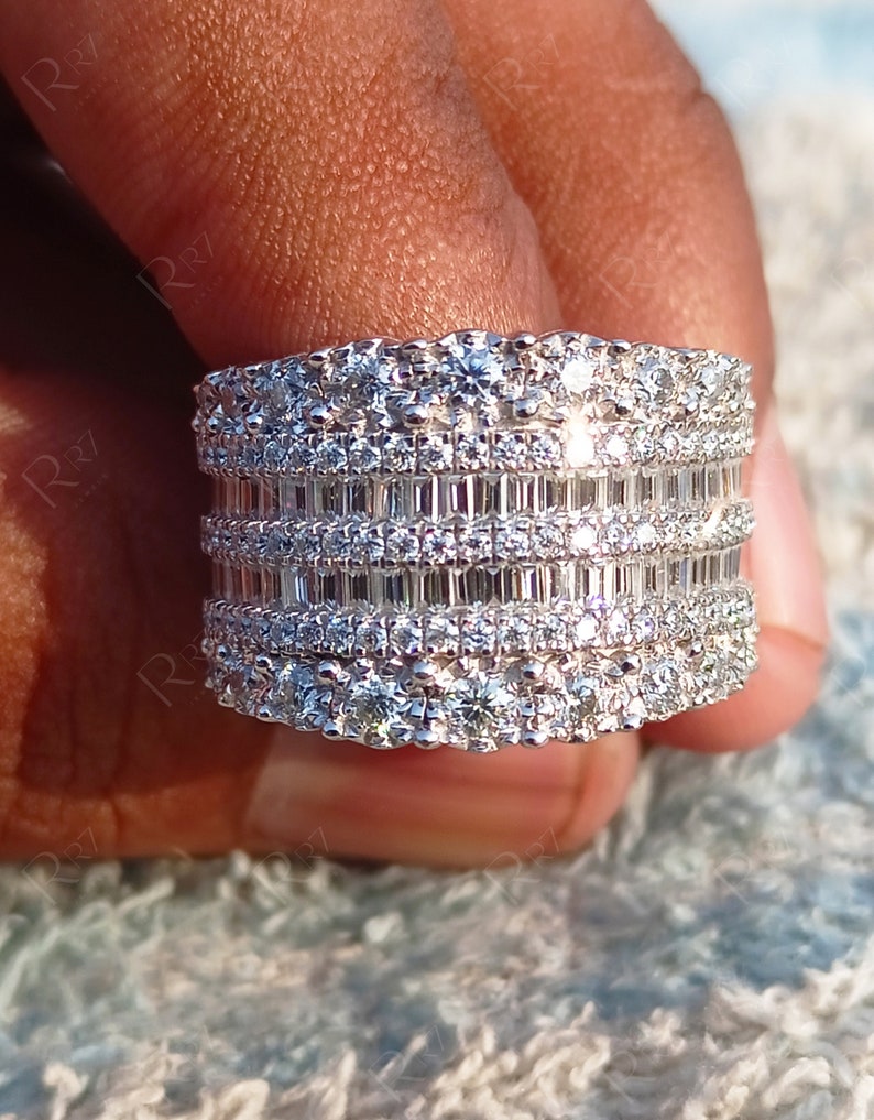 May include: A wide silver band ring with multiple rows of sparkling diamonds. The ring features a combination of round and baguette-shaped diamonds.