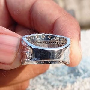 May include: A silver band ring with a row of small, clear stones set in a channel setting. The ring is shown from the side, with the stones facing the viewer.