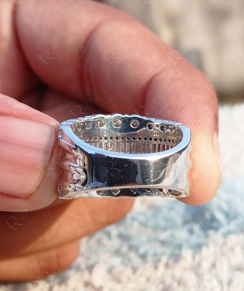May include: A silver band ring with a row of small, clear stones set in a channel setting. The ring is shown from the side, with the stones facing the viewer.
