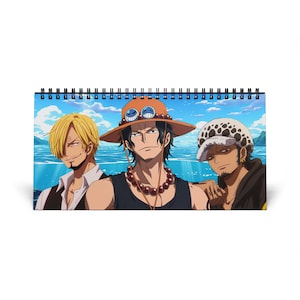 Puede incluir: Calendario de escritorio con espiral que presenta tres personajes de anime sobre un fondo de cielo azul y océano. Los personajes incluyen un hombre rubio con traje, un hombre con sombrero naranja y un hombre con sombrero blanco.
