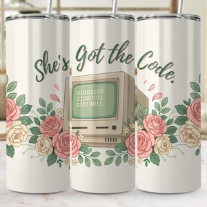 May include: A cylindrical tumbler with a white background featuring a vintage computer monitor displaying binary code. The design includes the text "She's Got the Code." and is decorated with clusters of pink and cream roses with green leaves.