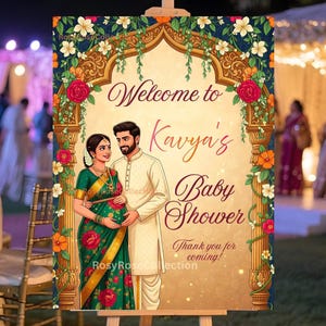 May include: A decorative sign on an easel with the text "Welcome to Kavya's Baby Shower". The sign features an illustration of a couple and is decorated with floral and gold accents. The background shows an outdoor event.