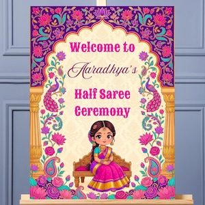 May include: A decorative sign on an easel with the text "Welcome to Aaradhya's Half Saree Ceremony." The sign features a cartoon illustration of a girl in a pink and gold saree, surrounded by floral and peacock designs in shades of purple, pink, and gold.