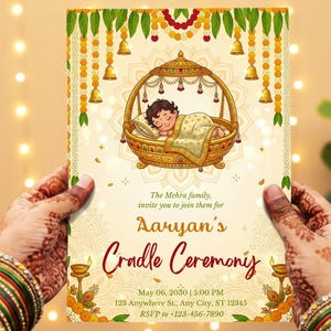 Puede incluir: Tarjeta de invitación a un baby shower, sostenida en manos, con una ilustración de una cuna dorada y un bebé durmiendo. La tarjeta está decorada con motivos florales y de campanas, y el texto dice "Ceremonia de la cuna de Aaryan".