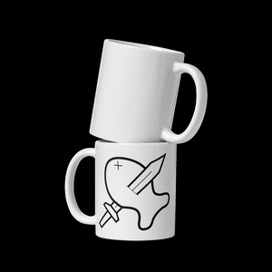 May include: Two white ceramic mugs stacked on top of each other. The top mug is empty. The bottom mug has a black and white graphic of a fish with a sword through it.