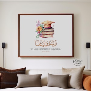 Puede incluir: Un cuadro enmarcado con una ilustración en acuarela de un birrete sobre libros, con flores. La impresión incluye caligrafía árabe y el texto en inglés "MY LORD, INCREASE ME IN KNOWLEDGE." La obra de arte está sobre un fondo blanco.