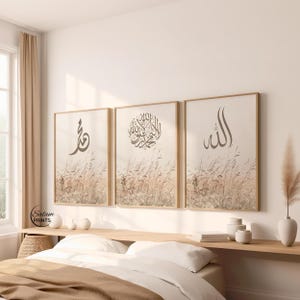 May include: Three framed wall art pieces with Arabic calligraphy. Each print features a different design in dark gray against a beige background with a wheat field illustration. The frames are a light wood color.