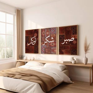 May include: Three framed wall art pieces with Arabic calligraphy. Each piece features a different design with a mix of red, brown, and blue colors. The artwork is displayed above a bed with a neutral-toned comforter.