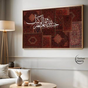 Może przedstawiać: Oprawiona grafika przedstawiająca patchwork z różnych czerwonych i brązowych wzorzystych dywanów. Biała arabska kaligrafia jest wyśrodkowana na grafice. Grafika jest wyświetlana na białej ścianie nad nowoczesnym salonem.