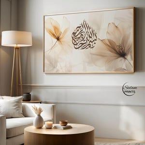 May include: A framed art print with a floral design in beige and brown tones. The artwork incorporates Arabic calligraphy in dark brown. The print is displayed in a contemporary living room setting, with a white sofa and a wooden coffee table. The overall aesthetic is modern.