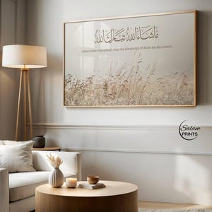Puede incluir: Una impresión artística enmarcada con un marco dorado. La obra presenta caligrafía árabe y el texto en inglés "What Allah has willed, may the blessings of Allah be abundant." El fondo muestra un campo de hierba alta.