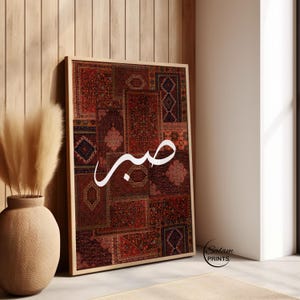 May include: Framed art print featuring a patchwork design of various rug patterns in shades of red, brown, and beige. The Arabic word "Sabr" is written in white script across the center. The print is displayed on a light-colored wall.