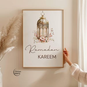 Puede incluir: Una impresión enmarcada con una ilustración de linterna dorada y detalles florales. Las palabras "Ramadan KAREEM" están escritas en escritura. La impresión está en un marco de madera.