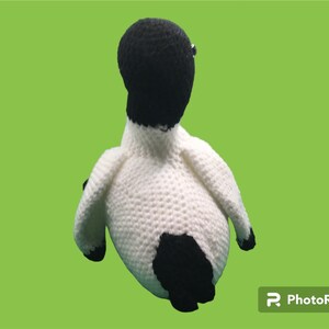 May include: A crocheted penguin toy with a white body and black head, wings, and tail. The penguin is sitting on a green background.