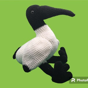 May include: A crocheted stuffed toy bird with a white body, black head, and black legs. The bird has a long, black beak and a black eye.