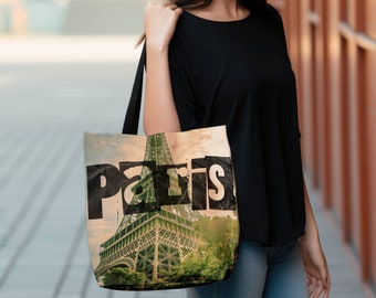 May include: A beige tote bag with a black and white graphic of the Eiffel Tower and the word "Paris" printed on it. The bag is being held by a person wearing a black shirt and blue jeans.