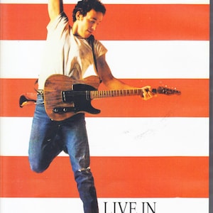 May include: DVD case for Bruce Springsteen's 'Live in Toronto 1984'. The cover features Springsteen playing a guitar against a red and white striped background. Text includes "BRUCE SPRINGSTEEN" and "LIVE IN TORONTO 1984".