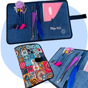 Puede incluir: Portafolio de tela azul con múltiples bolsillos, una cremallera y una cubierta estampada. El portafolio contiene un cuaderno rosa, bolígrafos, una pluma morada y otros artículos de papelería. El texto "Bilge N.H." es visible.