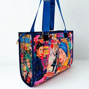 Może przedstawiać: Żywa torba typu tote z kolorowym wzorem pop-art z portretami i tekstem w stylu graffiti. Torba ma niebieskie wykończenia, uchwyty i zamek błyskawiczny ze złotym suwakiem. Wymiary torby nie są widoczne.