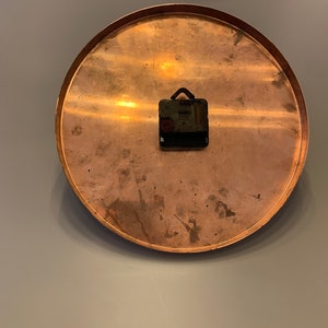 K&ouml;nnte beinhalten: Ein rundes Zifferblatt aus Kupfer mit einem schwarzen Uhrwerk, das an der R&uuml;ckseite befestigt ist.