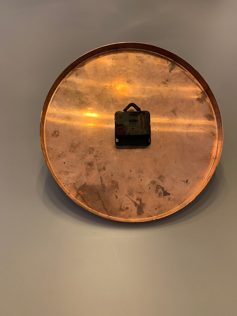 K&ouml;nnte beinhalten: Ein rundes Zifferblatt aus Kupfer mit einem schwarzen Uhrwerk, das an der R&uuml;ckseite befestigt ist.