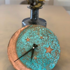 May include: A turquoise and copper colored clock with a crescent moon design and stars. The clock has black hands and a distressed finish.