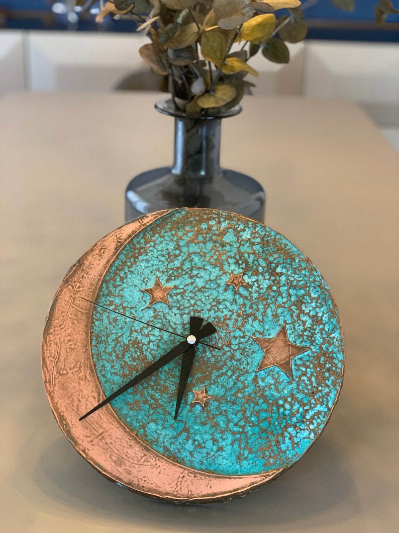 May include: A turquoise and copper colored clock with a crescent moon design and stars. The clock has black hands and a distressed finish.