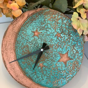 May include: A turquoise and copper clock with a crescent moon and stars design. The clock has black hands and a white face.