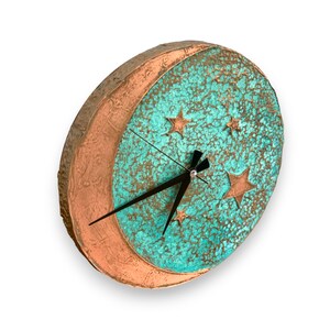 May include: A turquoise and copper colored clock with a crescent moon and stars design. The clock has black hands and a white background.