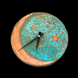 May include: A turquoise and copper clock with a crescent moon and stars design. The clock has black hands and a white face.