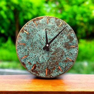 May include: A round, copper-toned clock with a distressed, textured surface. The clock face has black hands and copper-colored hour markers.