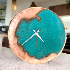 K&ouml;nnte beinhalten: Eine runde Uhr aus Kupfer und T&uuml;rkis mit wei&szlig;en Zeigern. Das Zifferblatt der Uhr hat eine abgenutzte, strukturierte Optik.