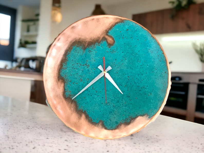K&ouml;nnte beinhalten: Eine runde Uhr aus Kupfer und T&uuml;rkis mit wei&szlig;en Zeigern. Das Zifferblatt der Uhr hat eine abgenutzte, strukturierte Optik.