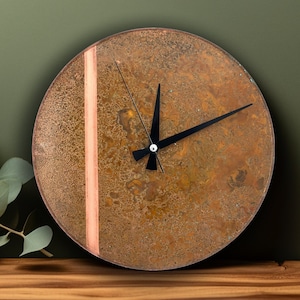May include: A round, rusty-brown clock with a copper-colored stripe and black hands. The clock is on a wooden surface.