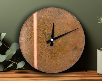 May include: A round, rusty-brown clock with a copper-coloured stripe and black hands. The clock is on a wooden surface.