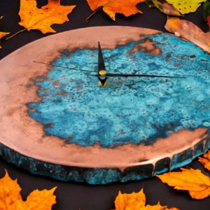 K&ouml;nnte beinhalten: Ein rundes, kupferfarbenes Zifferblatt mit einem blauen und gr&uuml;nen Harzdesign. Die Zeiger sind schwarz und das Zifferblatt hat einen rauen, strukturierten Rand.
