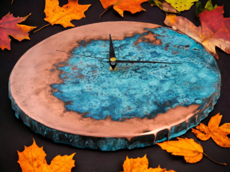 K&ouml;nnte beinhalten: Ein rundes, kupferfarbenes Zifferblatt mit einem blauen und gr&uuml;nen Harzdesign. Die Zeiger sind schwarz und das Zifferblatt hat einen rauen, strukturierten Rand.