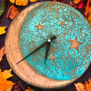 May include: A turquoise blue and copper clock with a crescent moon design and stars. The clock face has a distressed, textured look.