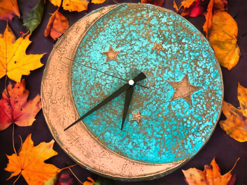May include: A turquoise blue and copper clock with a crescent moon design and stars. The clock face has a distressed, textured look.