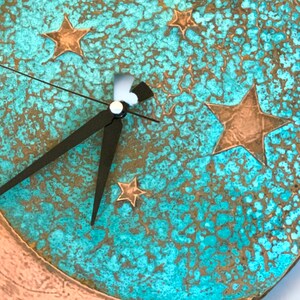 May include: A turquoise and copper clock with a crescent moon design and five stars. The clock hands are black.