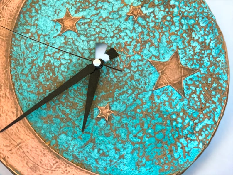 May include: A turquoise and copper clock with a crescent moon design and five stars. The clock hands are black.