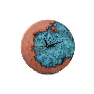K&ouml;nnte beinhalten: Eine runde, keramische Wanduhr mit einer kupfer- und blauen Glasur. Das Zifferblatt der Uhr hat schwarze Zeiger und eine goldene Mitte.