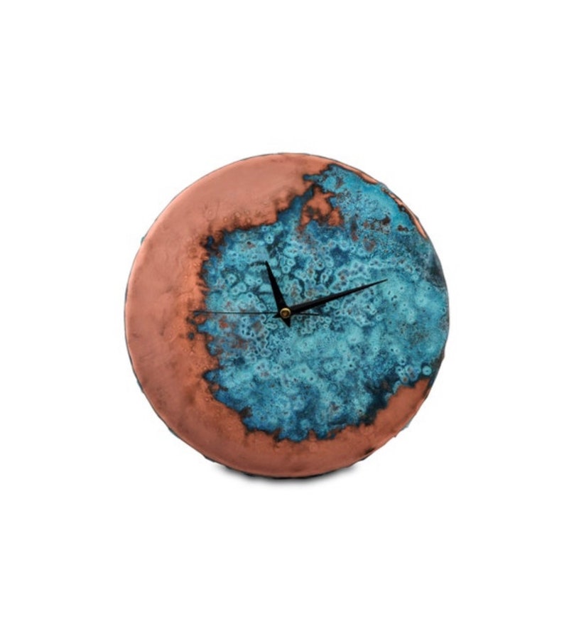 K&ouml;nnte beinhalten: Eine runde, keramische Wanduhr mit einer kupfer- und blauen Glasur. Das Zifferblatt der Uhr hat schwarze Zeiger und eine goldene Mitte.