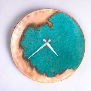 K&ouml;nnte beinhalten: Eine runde Wanduhr in T&uuml;rkis und Kupfer mit wei&szlig;en Zeigern. Das Zifferblatt der Uhr hat eine strukturierte, marmorierte Optik.