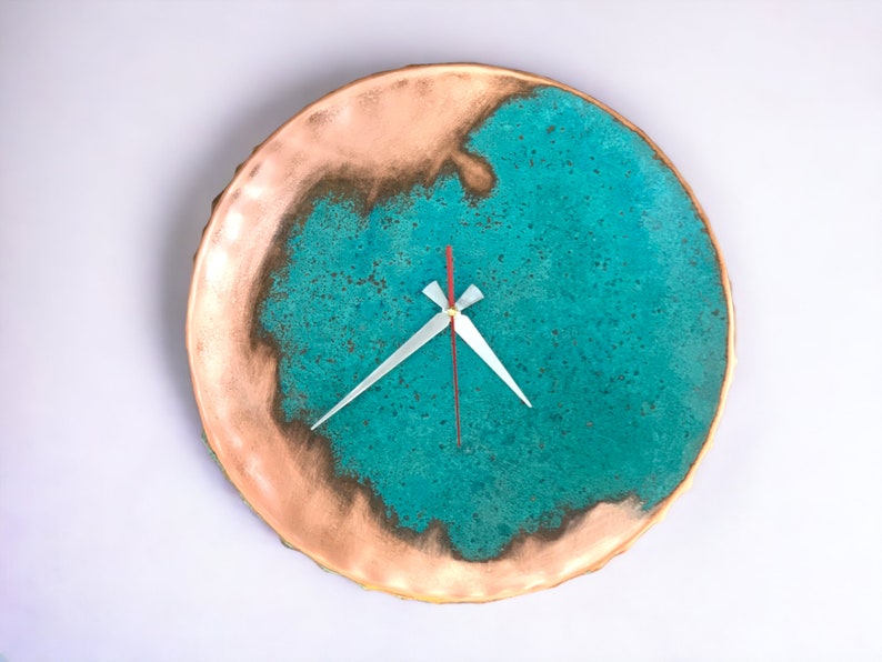 K&ouml;nnte beinhalten: Eine runde Wanduhr in T&uuml;rkis und Kupfer mit wei&szlig;en Zeigern. Das Zifferblatt der Uhr hat eine strukturierte, marmorierte Optik.