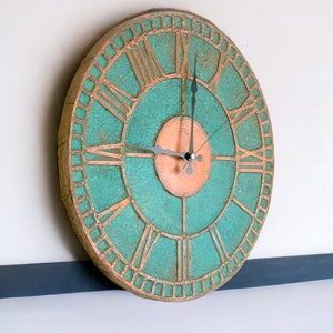 May include: A large, round, teal and copper wall clock with Roman numeral markings. The clock has a copper center and black hands.
