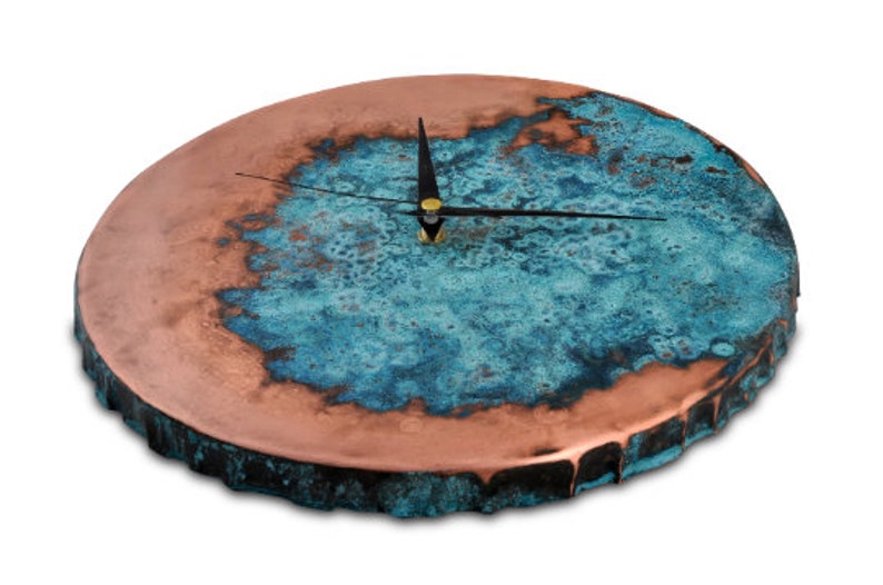 K&ouml;nnte beinhalten: Eine runde Kupferuhr mit einer blauen und gr&uuml;nen Patina. Das Zifferblatt der Uhr hat schwarze Zeiger und eine goldene Mitte.