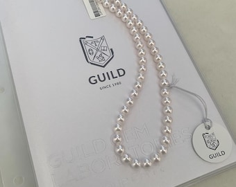 May include: A double-strand white pearl necklace featuring a dark floral-shaped clasp with a gold center. The necklace is displayed on a Guild Gem Laboratories document with a white circular tag attached, featuring the Guild logo and text.