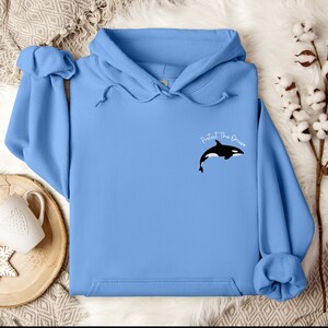May include: A light blue hoodie with a black and white orca graphic and the text "Protect The Ocean" on the front.